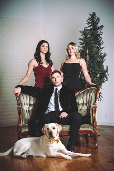 two women and a man sitting on a couch with a dog in front of them