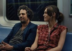 a man and woman sitting on a subway train looking at each other with ear buds in their ears