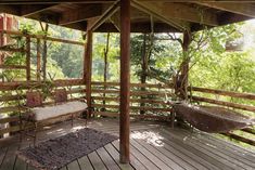 a wooden deck with two hammocks on it and trees in the back ground