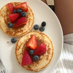 two pancakes topped with strawberries and blueberries on a white plate