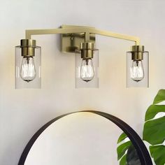 three light bathroom fixture with clear glass shades and brass finish, on a white wall