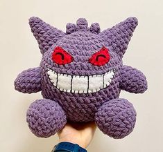 a hand holding up a purple knitted monster head with red eyes and teeth on it's face