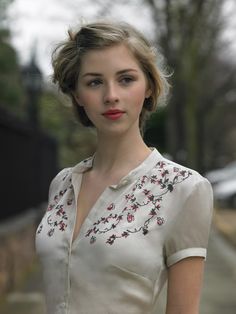 a woman with short hair wearing a white shirt and red lipstick posing for the camera