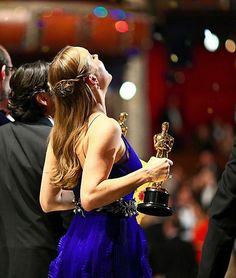 a woman in a blue dress holding an award and looking up at the sky with her eyes closed