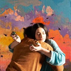 a woman holding onto a stuffed animal in front of a colorful wall with birds on it