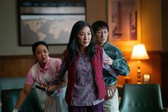 three people standing in a living room with one holding a remote and the other pointing at something