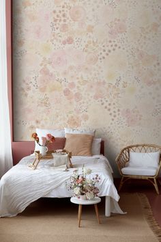 a white bed sitting under a window next to a wall covered in pink and yellow flowers