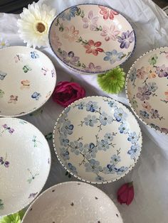 several bowls with flowers on them sitting on a white table cloth next to a flower