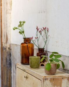 three vases and two cups are sitting on a dresser