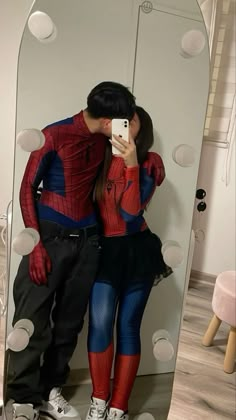 a man and woman dressed as spider - man taking a selfie in front of a mirror