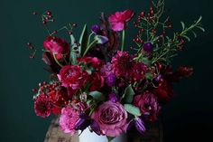 a white vase filled with lots of purple and red flowers on top of a wooden table