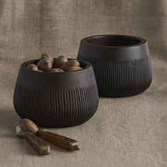 two black bowls filled with nuts on top of a brown cloth covered table next to cinnamon sticks