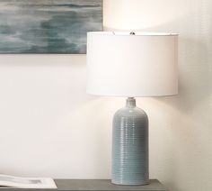 a blue vase sitting on top of a wooden table next to a white lampshade