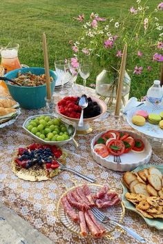 a table filled with lots of food on top of a grass covered field next to flowers