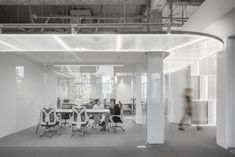 an office with people sitting at desks in the middle of it, and one person walking by