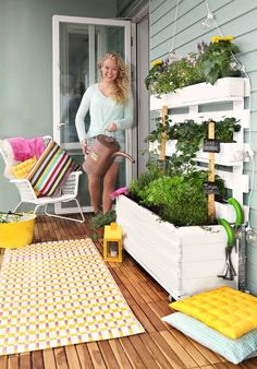 a woman is standing on the porch next to some plants and potted planters