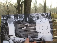 an old photo of two people sitting on a bench in a park with trees behind them