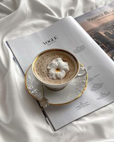 a cup of hot chocolate on top of a saucer next to an open magazine