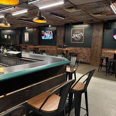 an empty bar with several stools and tables in front of the bar, as well as television screens on the wall