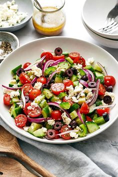 a salad with cucumbers, tomatoes, olives and feta cheese in a white bowl