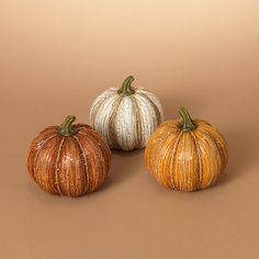 three small pumpkins sitting next to each other on a brown surface with one orange and the other white