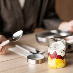 a person sitting at a table with some food in a jar and spoon next to it