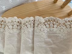 four white curtains with lace on them hanging from a wooden rail