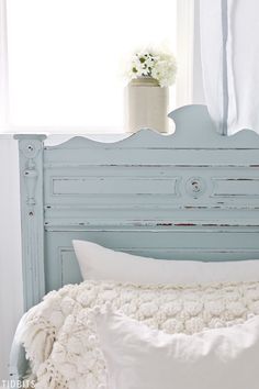 a blue headboard with white pillows and a vase full of flowers on the window sill