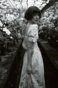 a woman is standing in a greenhouse wearing a dress and holding her hand on her hip