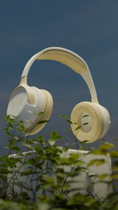 two white headphones sitting next to each other on top of a plant covered ground