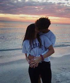 a man and woman kissing on the beach at sunset