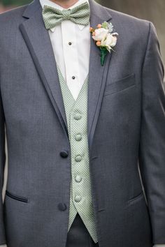 a man wearing a gray suit and green bow tie with a white rose in his lapel