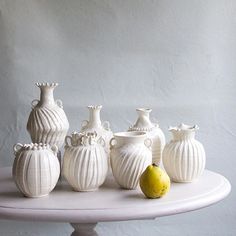 five white vases sitting on top of a table next to a pear and an apple