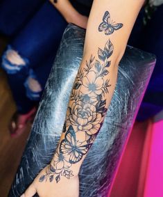 a woman's arm with flowers and butterflies tattoo on her left hand, sitting on a chair