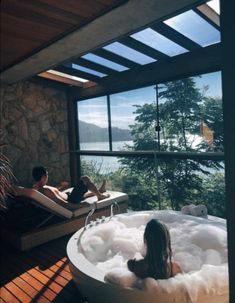 two people relaxing in the jacuzzi tub overlooking the lake and mountains, while another person sits on the deck