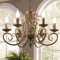 a chandelier hanging from the ceiling in a room with windows and potted plant