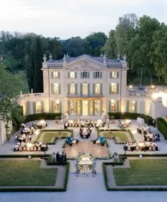 an aerial view of a large white house with lots of greenery and people sitting at tables in the front yard