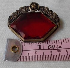 "For your consideration we have a lovely lapel pin/brooch from the Victorian era. This pin is stunning in detail and color, done with bright red glass stone and bordered on the top by a floral design of brass. We believe this pin was upcylced from a possible shoe buckle. Measuring approximately 1.5\" long and 1.25\" tall, this is a great accessory for any dapper gent or well turned out woman. Shipping policies: If you choose to pay via Paypal, you must either be a verified buyer, or provide a co Handmade Vintage Red Brooches, Vintage Red Lapel Pin For Gift, Vintage Red Lapel Pin As Gift, Red Vintage Lapel Pin For Gift, Red Vintage Lapel Pin As Gift, Antique Red Brooch As Gift, Antique Red Brooches As A Gift, Antique Red Brooches For Gift, Antique Red Brooches As Gift