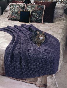 a cat laying on top of a bed covered in a purple blanket and throw pillow