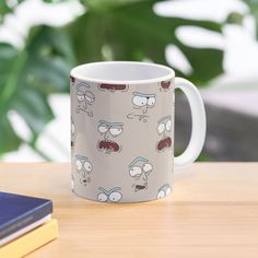 a coffee mug sitting on top of a wooden table next to a book and plant