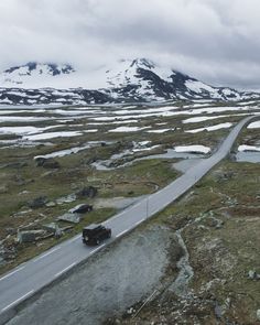 a car driving down a road in the middle of snow covered hills and grass with mountains in the background