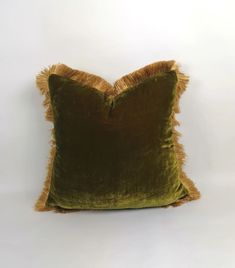 a green velvet pillow with tassels on the bottom and sides, against a white background