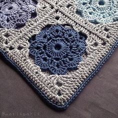 a crocheted square with blue and white flowers on it, sitting on top of a bed