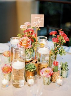 a table topped with lots of vases filled with flowers and candles next to each other