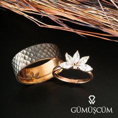 two gold wedding rings sitting next to each other on top of a black surface with grass in the background