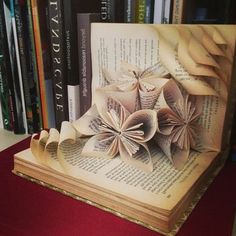 an open book with folded paper flowers on it and some books in the back ground