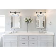 a white bathroom with double sinks and two mirrors on the wall next to each other