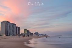 people are walking on the beach at sunset near some hotels and condos in the background