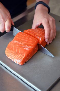 a person is cutting up some fish on a metal counter top with a large knife