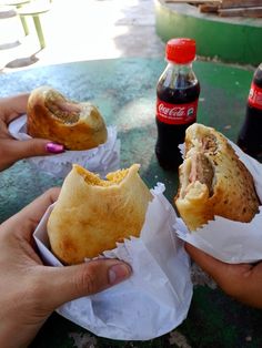 two people holding sandwiches in their hands with coca cola bottles on the table behind them